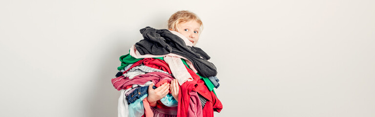 Fototapeta Mommy little helper. Adorable funny child arranging organazing clothing. Kid holding messy stack pile of clothes things. Home chores housework for kids. Web banner header. obraz