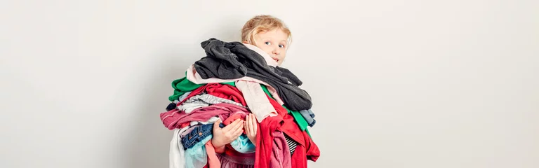 Fotobehang Mommy little helper. Adorable funny child arranging organazing clothing. Kid holding messy stack pile of clothes things. Home chores housework for kids. Web banner header. © anoushkatoronto