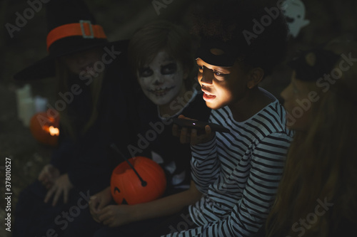 Multi-ethnic group of kids telling scary stories on Halloween, focus on African-American boy holding flashlight in foreground