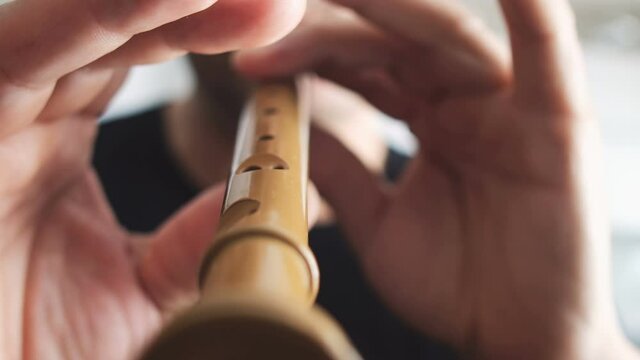 Close-up of a man playing on a recorder on a blur background, wooden wood flute