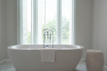 Minimalist luxury Bathtub with traditional faucets in front of opened venetian blinds