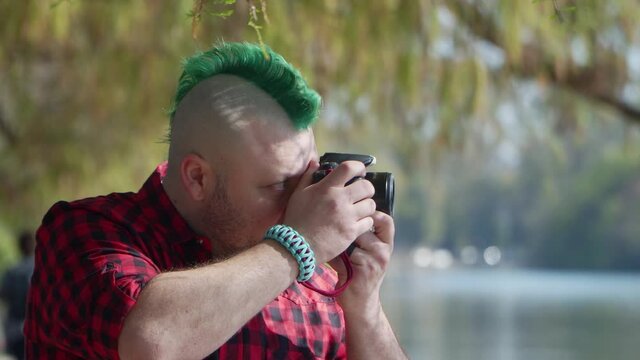 An alternative man with a green mohawk taking a photo with his camera at park