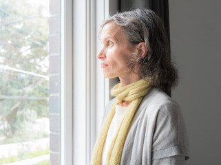 Close up profile of  middle aged woman lwith grey hair ooking out of window (selective focus)