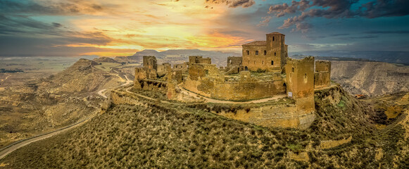Dramatic aerial sunset view of Montearagon castle near Huesca Spain, with partially restored walls and towers on a bare hilltop © tamas