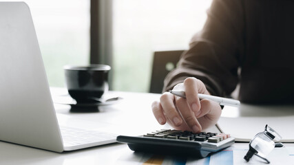Fototapeta premium Close up Business woman using calculator and laptop for do math finance on wooden desk in office and business working background, tax, accounting, statistics and analytic research concept