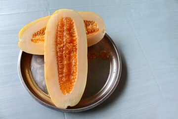 Honeydew melon (cucumis melo), two halves slice in stainless steel tray on gray wallpaper background closeup.