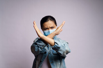 Asian woman wearing protective face mask showing arms crossed making stop sign isolated over white...