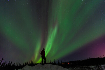 Naklejka na ściany i meble Silhouette man standing on mound under northern lights Alakska. Auroras display dynamic patterns of brilliant lights that appear as curtains, rays, spirals, or dynamic flickers covering the entire sky