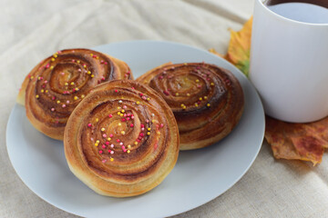 fresh baked cinnamon rolls or buns with sugar sprinkle topping on white plate and cup of black tea on table, view from angle above, lifestyle stock photo image background