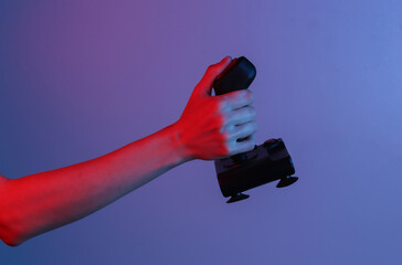 Hands holding retro joystick in blue-red neon gradient light. Old gaming. 80s retro wave