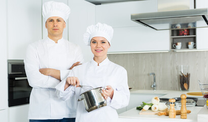 Portrait of female and male cooks who are standing with devices on their work place in the kitchen at the cafe.