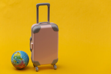 International travel concept. Mini pink plastic travel suitcase with globe on yellow background. Minimal style