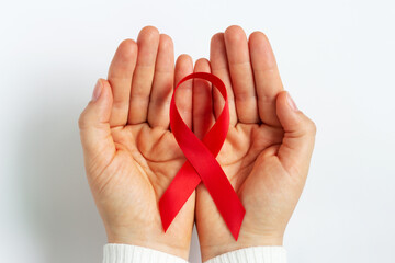 Female hands hold a red ribbon on white background top view.