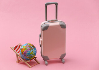 Travel or Beach trip concept. Mini travel suitcase and dack chair with globe on pink background. Minimal style