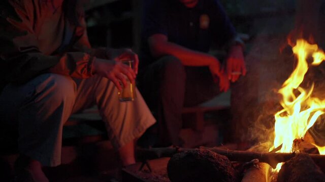 Blurred motion of woman with boyfriend sitting on cottage terrace above bonfire with talking and drinking alcohol. Couple enjoy outdoor lifestyle together. Holiday vacation travel and camping concept.