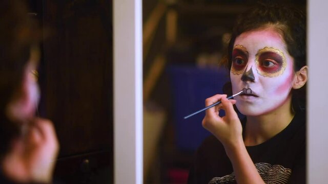 Mujer joven mexicana latina maquillaje catrina calavera d&iacute;a de muertos halloween frente al espejo tradicional festividades colorido esqueleto cara rostro blanco close-up