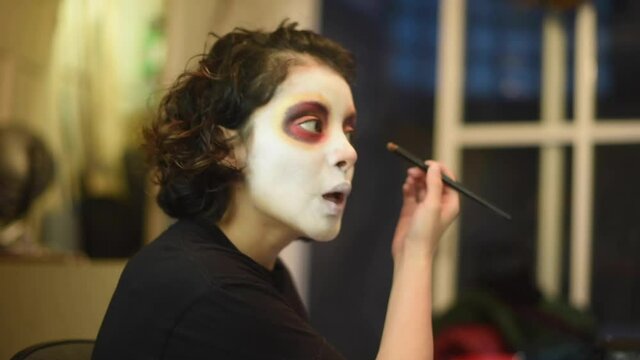 Mujer joven mexicana latina maquillaje catrina calavera día de muertos halloween frente al espejo tradicional festividades colorido esqueleto cara rostro blanco close-up