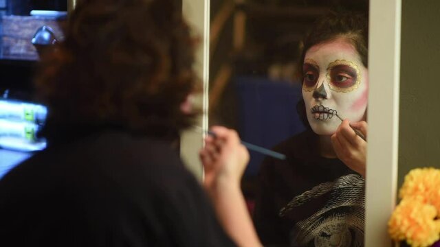 Mujer joven mexicana latina maquillaje catrina calavera d&iacute;a de muertos halloween frente al espejo tradicional festividades colorido esqueleto cara rostro blanco close-up