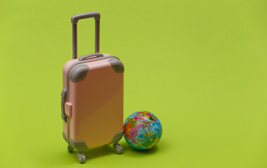 International travel concept. Mini plastic travel suitcase and globe on green background. Minimal style