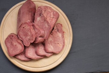 Beef tongue.Meat offal. Cold meat appetizer. Beef tongue slices close-up on wooden round board on black slate background.protein product