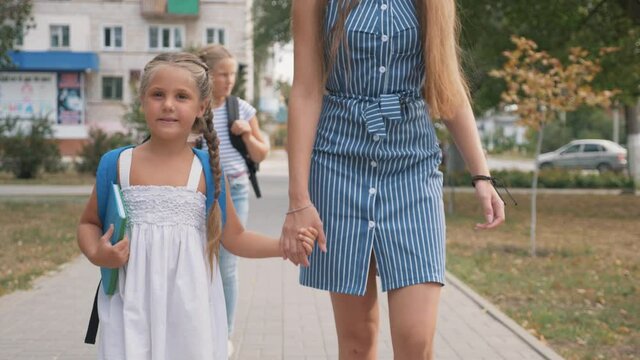 Happy family mom and daughter go hand in hand. A woman and a girl with a backpack behind them. Happy little girl dreams of school. Dreaming little girl goes with mom to school for the first lesson