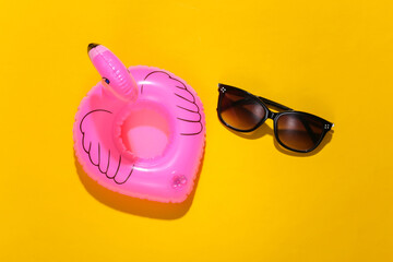 Inflatable pink flamingo with sunglasses on yellow sunny background. Summer vacation concept....