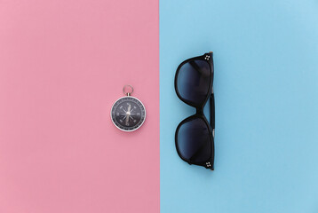 Minimalism travel, adventure flat lay. Sunglasses and compass on blue-pink pastel background. Top view