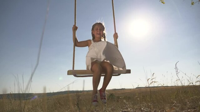 Amusement park dream concept. Happy girl swinging on a swing in the park at sunset. child plays with wooden swing, childhood dream, airplane pilot flights to the sky. A happy family