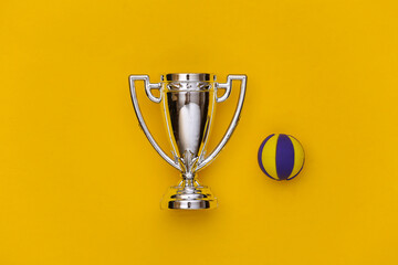 Mini volleyball ball and champion cup on yellow background. Minimalism Sport concept. Top view. Flat lay