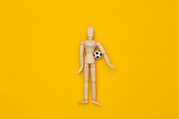 Mini wooden puppet holding a soccer ball on a yellow background