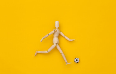 Mini wooden puppet running with a soccer ball on a yellow background