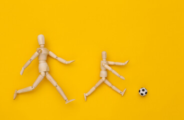 Two wooden puppet playing soccer with a ball on yellow background