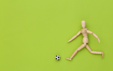Wooden puppet playing soccer with a ball on green background