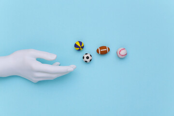 White mannequin hand and mini balls of different sports on a blue background. Top view © splitov27