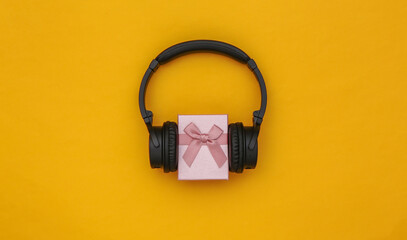 Stereo headphones and gift box on a yellow background. Music lover