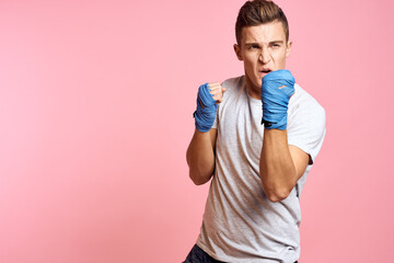 Fototapeta na wymiar Guy in blue gloves on a pink background are boxing in a white t-shirt cropped view