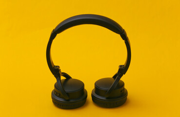 Black stereo headphones stand on yellow background