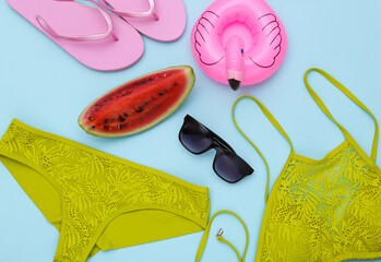 Slice of ripe watermelon and swimsuit, beach accessories on blue background. Summer fun, beach rest. Top view. Flat lay