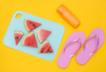 Sliced slices of ripe watermelon on a blue board, beach accessories. Yellow background. Summer time. Top view. Flat lay