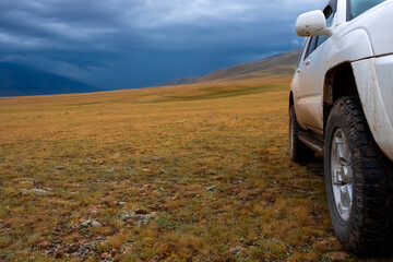 Fototapeta na wymiar Offroad suv car on moutain plateau with mountains and rain clouds background. Summer vacation, travel concept. Borokhudzir plateau, tourism in Kazakhstan concept.
