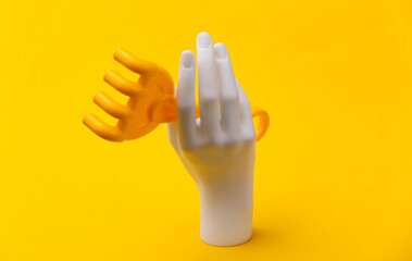 White mannequin hand holds toy rake on yellow background