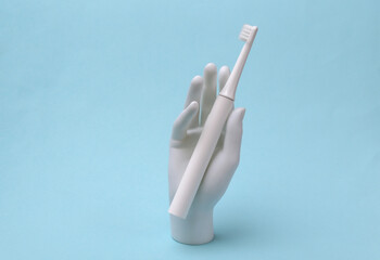 White mannequin hand holding electric toothbrush on blue background