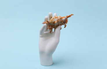 White mannequin hand holds seashell on blue background