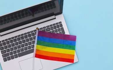 Laptop and LGBT rainbow flag on blue background. Gay parade, freedom, tolerance