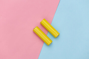 Two yellow AA batteries on pink blue pastel background. Top view
