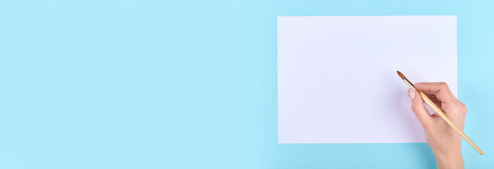 Hand with paint brush on blue background. Flat lay, overhead view image. Copy space, template.