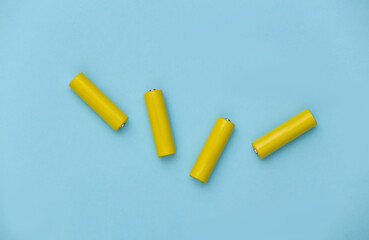 Four yellow AA batteries on blue pastel background. Top view