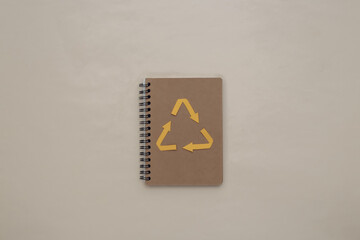 Recycled arrows sign and notebook on beige background. Eco concept. Top view