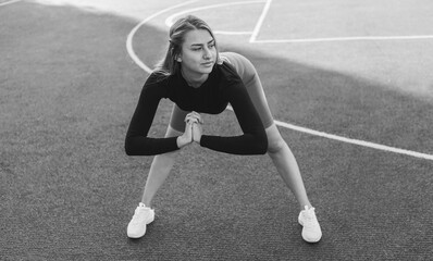 Young attractive woman in sportswear doing pre-training warm-up, body stretching at the stadium. Healthy lifestyle concept.