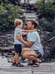 Father hugs son sitting squatting, look each other, smile. Happy childhood, fathers day, mountain,...